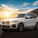 White BMW X3 parked in front of a sunset on a mountain