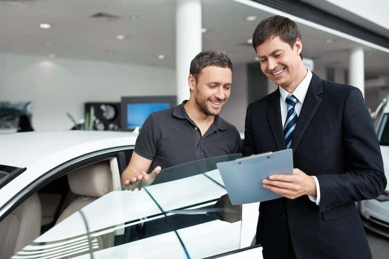 Two men standing by a car going over forms