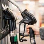 A person reaches for a fuel pump at a gas station