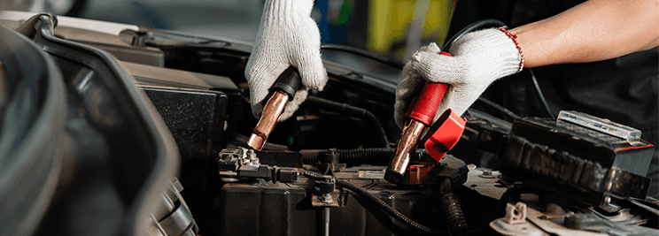Everything You Need to Know about Your Car Battery at Carolina CDJR | Person with white gloves about to connect jumper cables to battery located in the engine bay