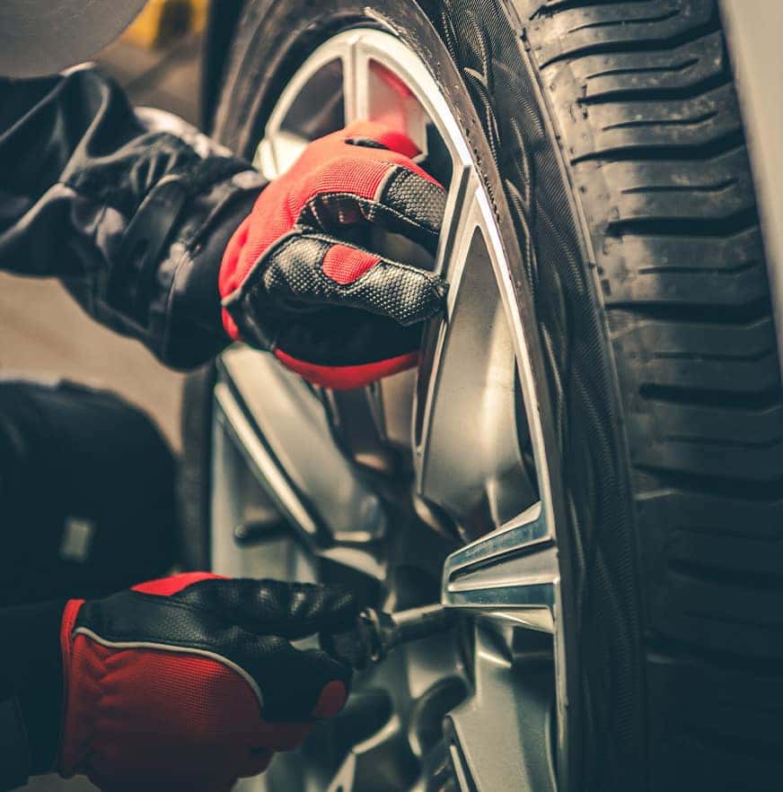 What is a Tire Rotation? at Carolina Chrysler Dodge Jeep RAM | Close-Up Shot of Service Technician Tightening Bolts on Tire