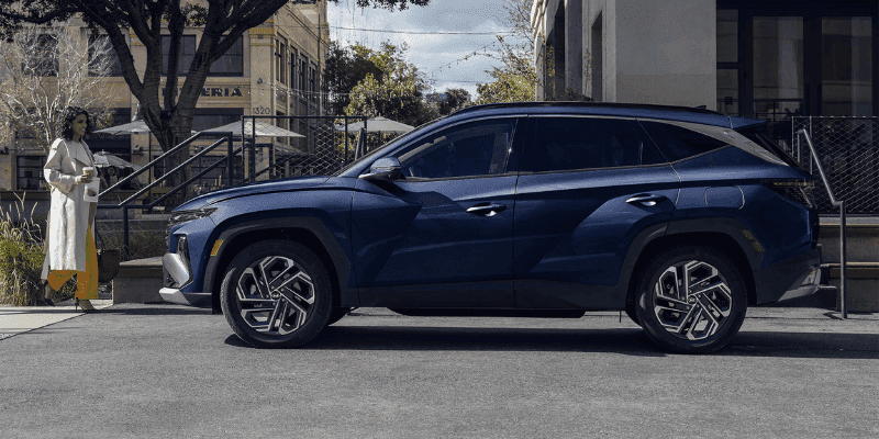 Blue Hyundai Tucson parked on a city street with a woman walking nearby