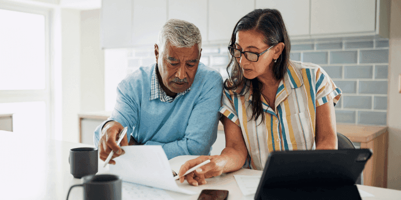 Couple reviewing documents together at a kitchen table with a tablet nearby
