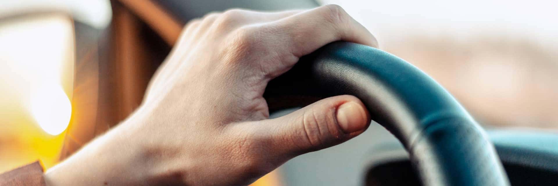Close up of male hand on steering wheel at dusk