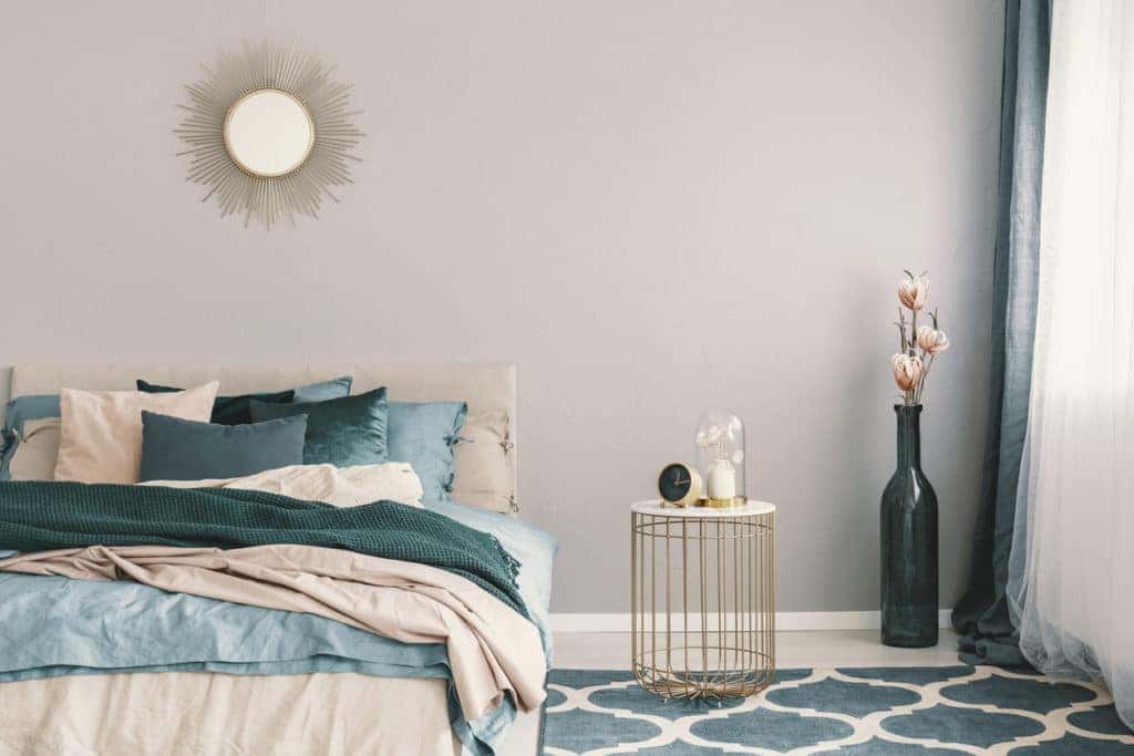 Clock and flower in fancy vase on nightstand table next to king size bedroom with emerald green and beige bedding