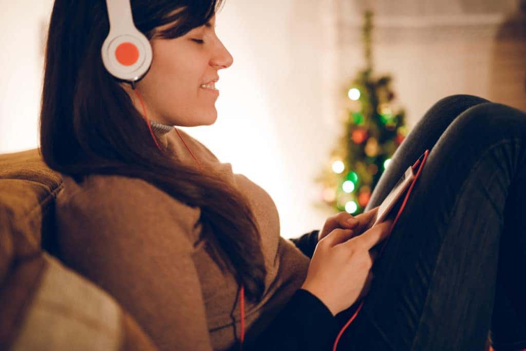 woman listening to music over headphones at home with Christmas tree