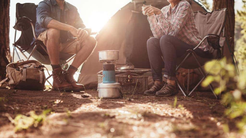 couple camping outside tent with gas stove at glaring sunrise