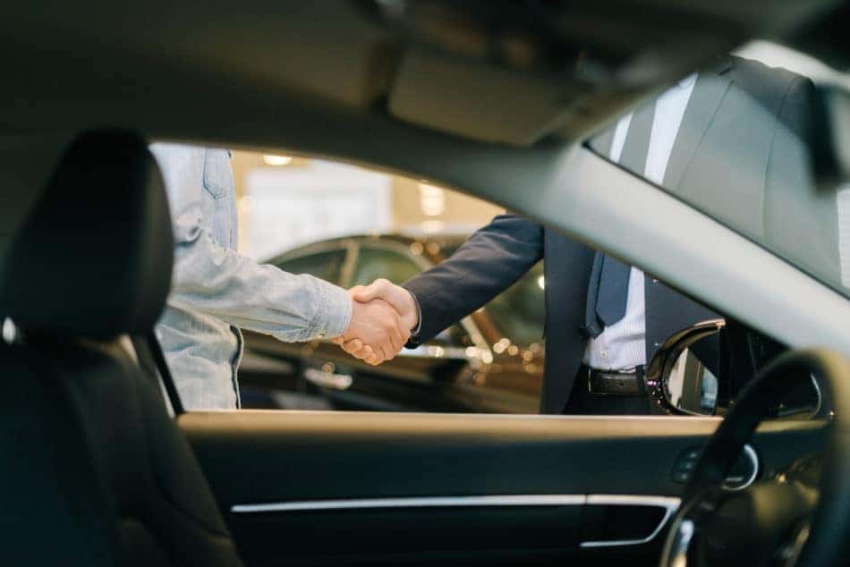 Buyer of car shaking hands with seller in dealership