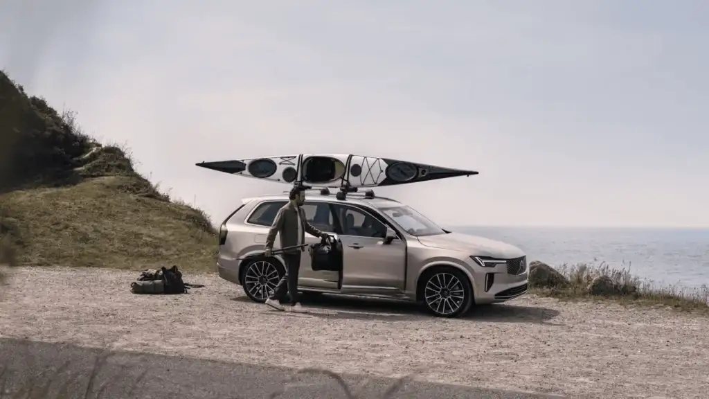2025 Volvo XC90 SUV with roof-mounted kayak near the coast, showcasing powertrain options and performance capabilities.