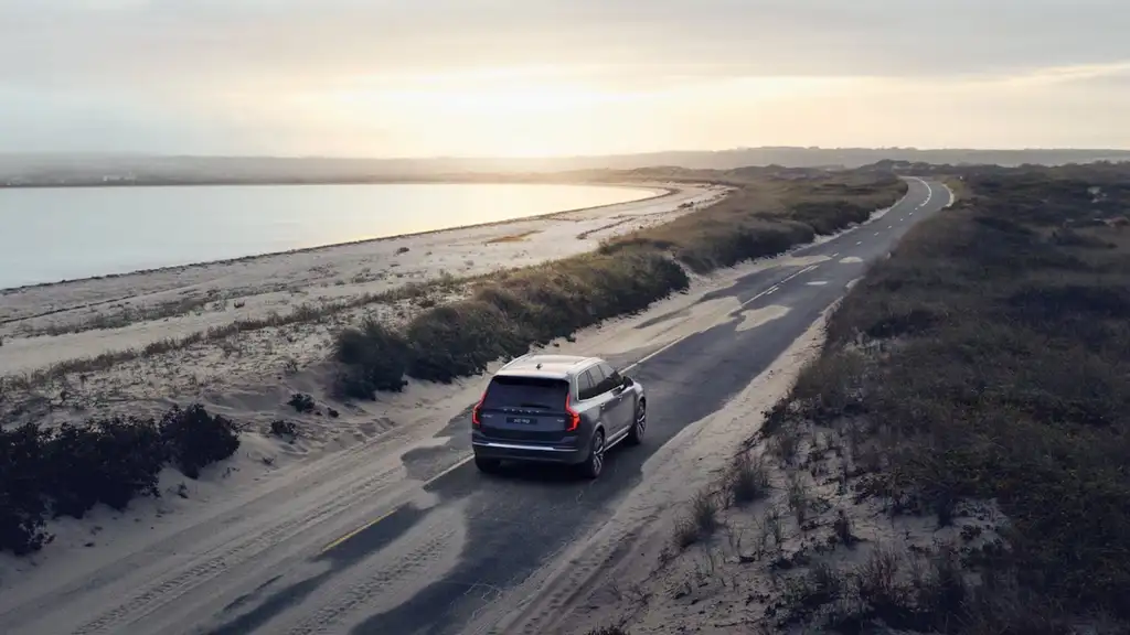 2025 Volvo XC90 Plug-In Hybrid driving along a scenic coastal road at sunset, ideal for Bristol TN family holiday travel.