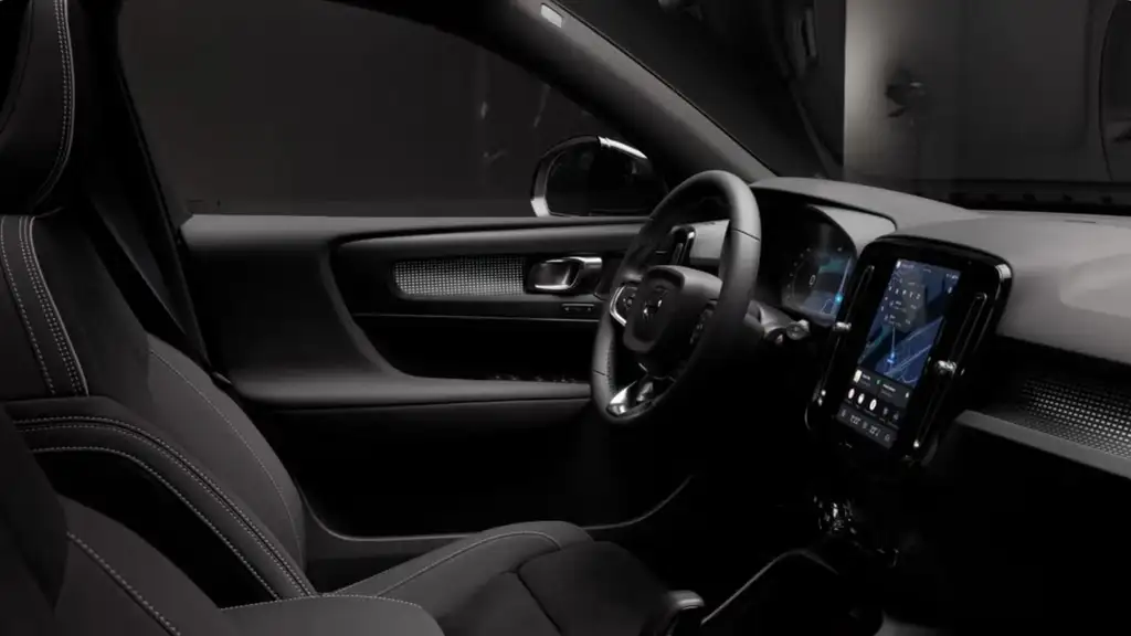 Dark interior view of the 2026 Volvo XC40 showcasing the driver seat, steering wheel, digital display, and modern infotainment interface.