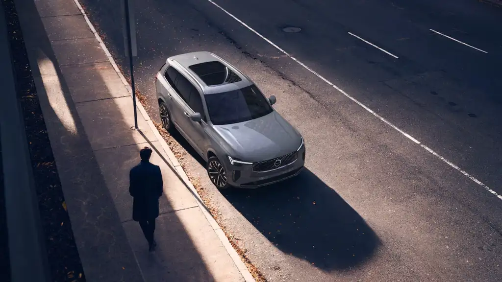 Overhead exterior view of a 2026 Volvo XC90 parked along a city street, showcasing roof design, sunroof, and sleek SUV proportions.
