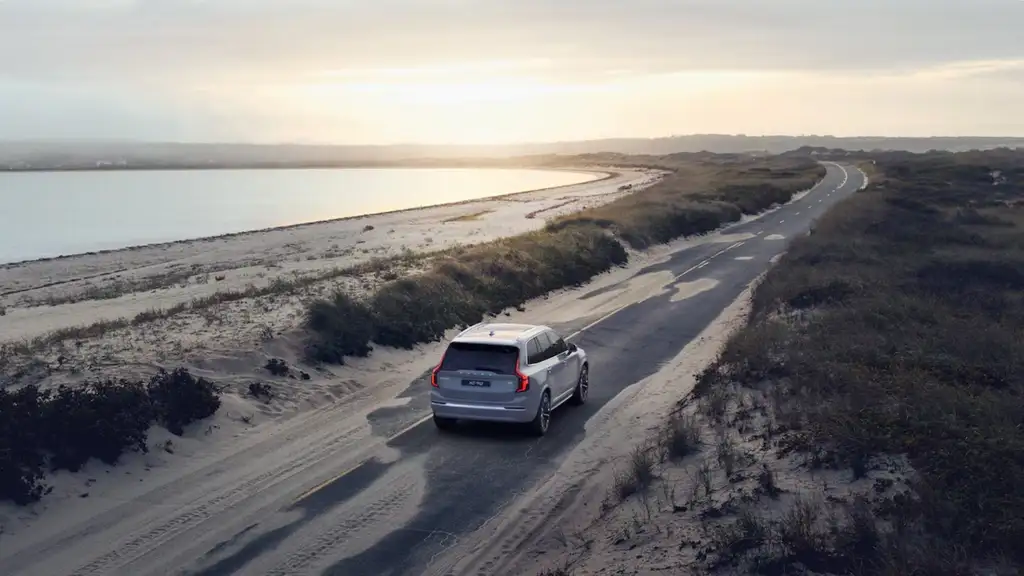 2026 Volvo XC90 driving along a coastal road at sunrise, showcasing winter-ready performance and safety features for Bristol, TN drivers.
