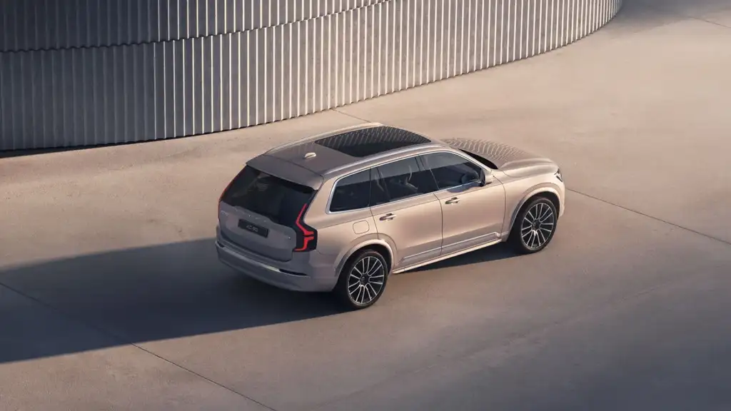 Overhead rear view of a beige 2026 Volvo XC90 Plug-in Hybrid driving near Kingsport, TN, highlighting luxury SUV design and panoramic roof.