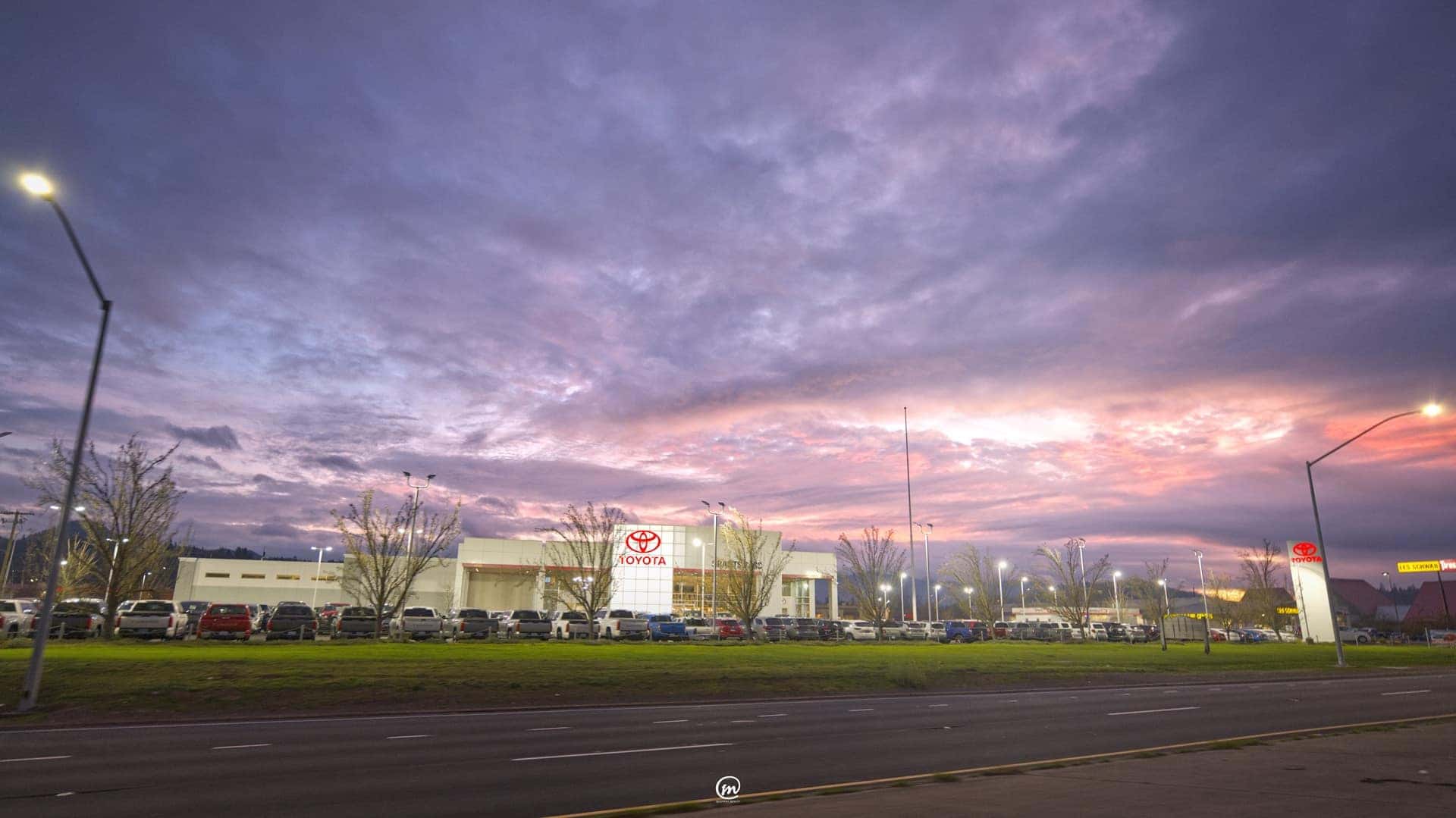 Toyota dealership building and a lot of parked vehicles across a highway under a pink and purple sunset sky