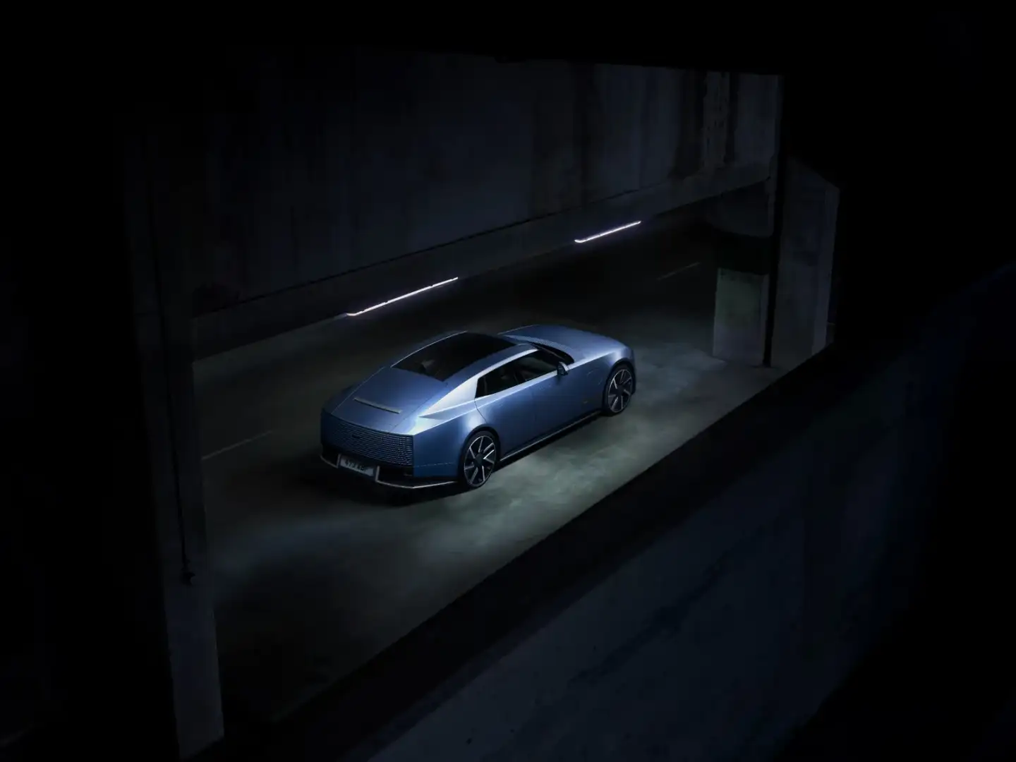 Blue Jaguar Type 01 electric GT shown from above at a rear three-quarter angle in a dimly lit parking garage