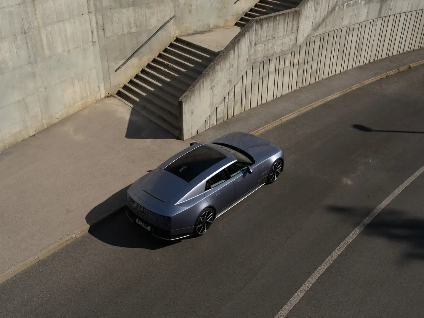 Aerial view of a blue Jaguar Type 01 with panoramic glass roof parked beside concrete stairs