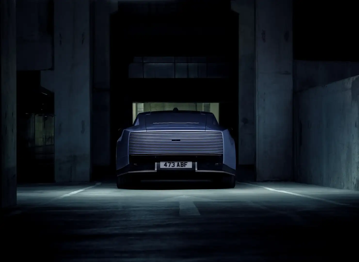 Rear view of a blue Jaguar Type 01 showing the full-width louvered tail in a dark garage
