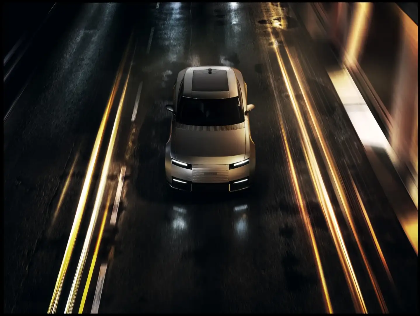 Overhead front view of a silver Jaguar Type 01 driving at night with light trails