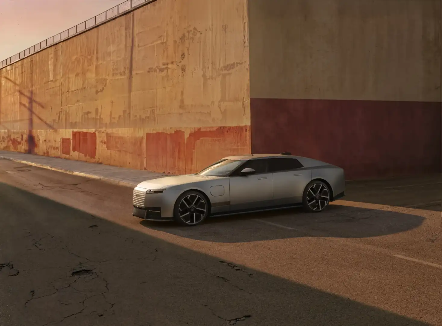 Silver Jaguar Type 01 electric GT parked by an orange wall at sunset