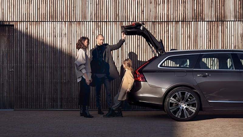 A family of 3 standing rear of a Volvo vehicle