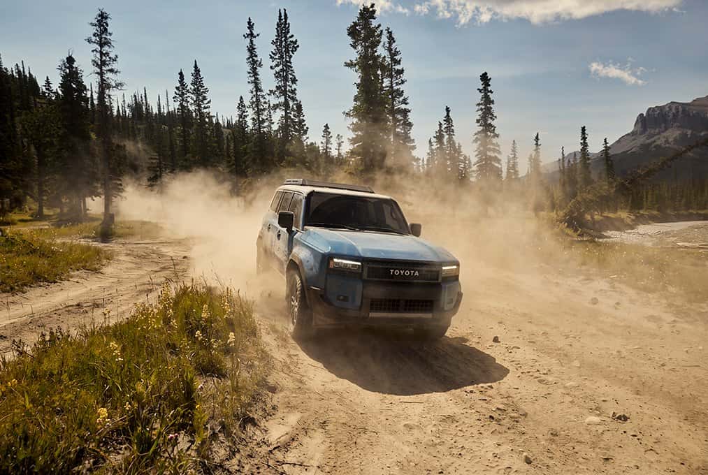 Blue 2027 Toyota Land Cruiser driving on a dirt forest road, available at Joseph Airport Toyota in Vandalia, Ohio