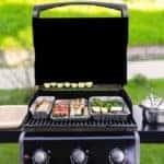 An opened gas grill with vegetables, meat, and sausages.