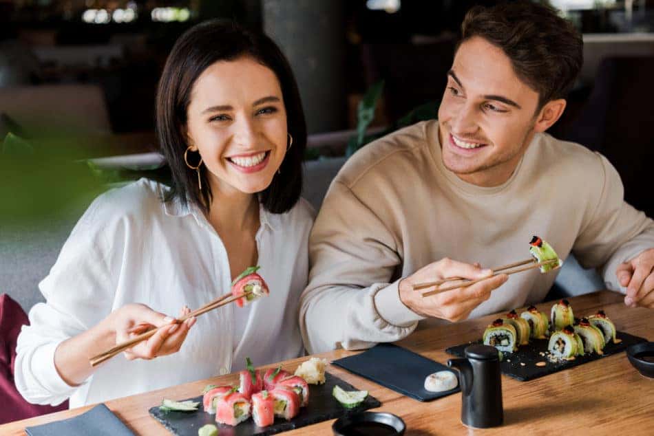Happy couple eating sushi with chopsticks