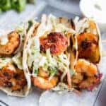 Grilled jumbo shrimp in corn tortilla tacos with cabbage garnish on an old fashioned newspaper wrapper.
