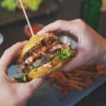 man holds burger with hands and sweet potato fries