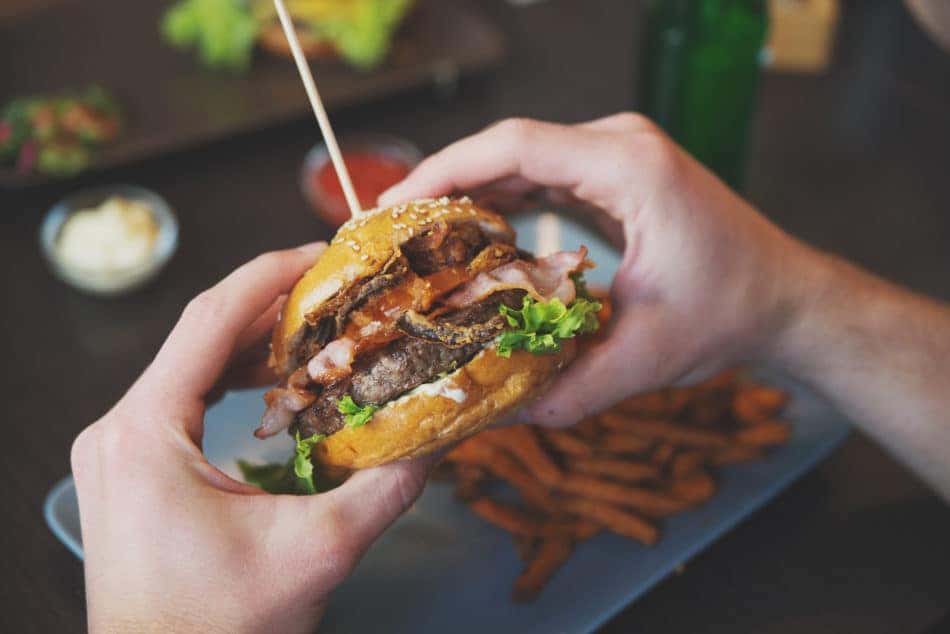 man holds burger with hands and sweet potato fries