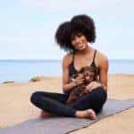 Smiling woman sitting with her dachshund on a yoga mat by the ocean