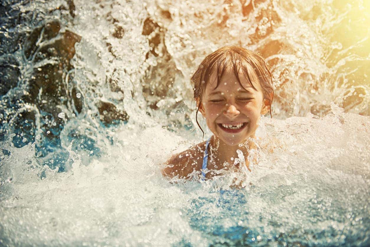 ittle girl playing in waterfall in waterpark swimming pool