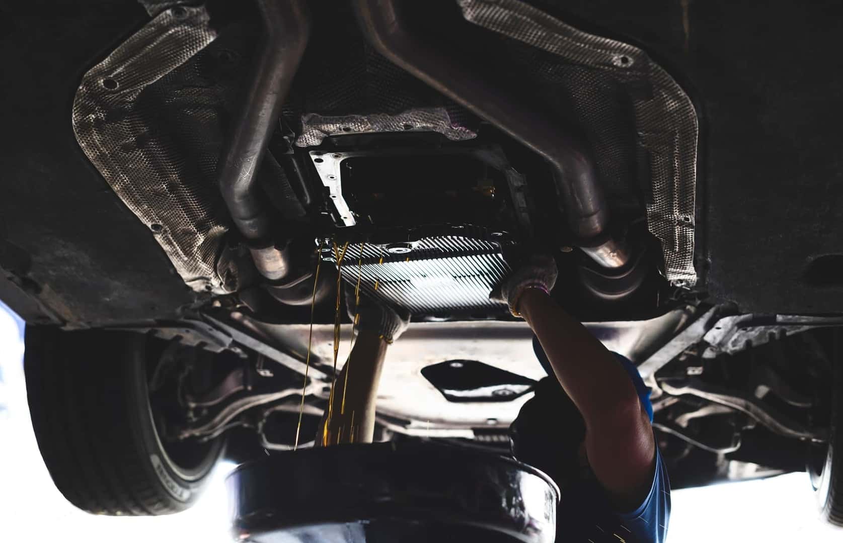A mechanic is performing a transmission repair service. The image provides a close-up view of the vehicle’s undercarriage, exhaust components, and transmission area.