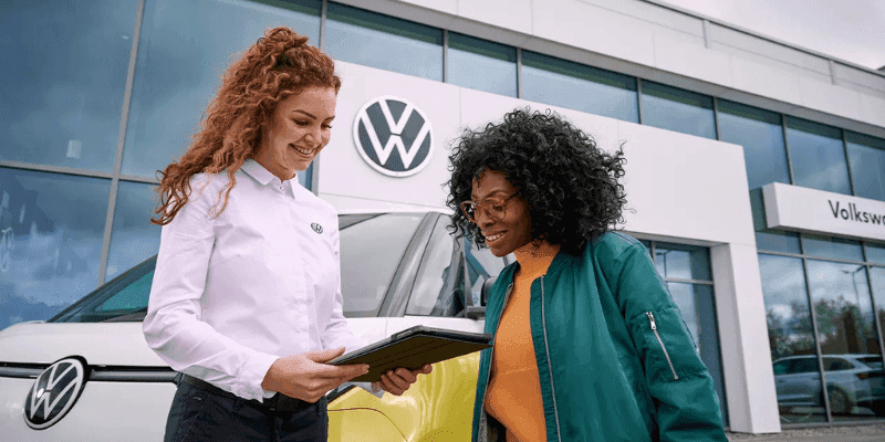Volkswagen sales rep reviewing a tablet with a customer outside a VW dealership
