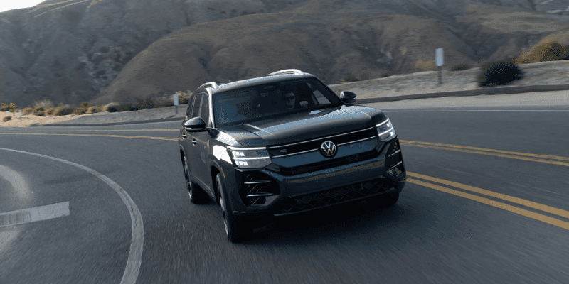 Dark gray Volkswagen Atlas SUV driving on a winding road with desert mountains in the background