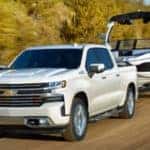 2019 Chevrolet Silverado 1500 in white hauling a boat on a dirt road