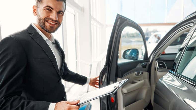 The Advantages of Buying a Car from a Dealership vs. a Private Seller. Learn more at Stetler DCJR in York, PA | Sales man opening the door to a new car while holding on to a clipboard