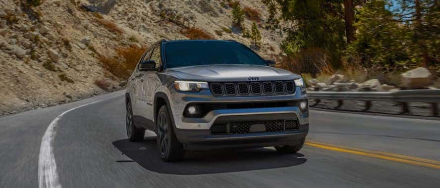 A silver Jeep Compass driving around a bend on the road.