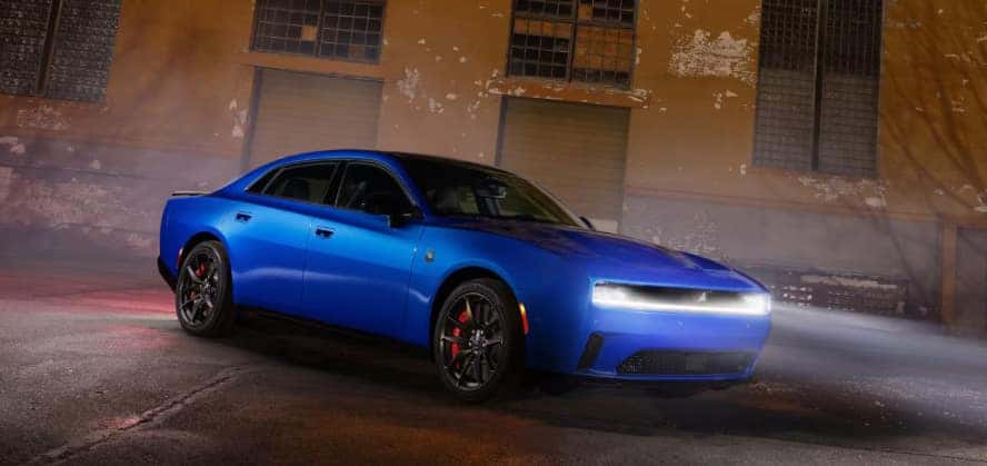 A blue Dodge Charger with its headlights on in a warehouse.