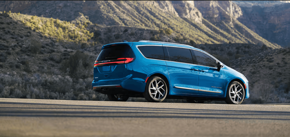 A lower angle side view of a blue Chrysler Pacifica near a mountain.