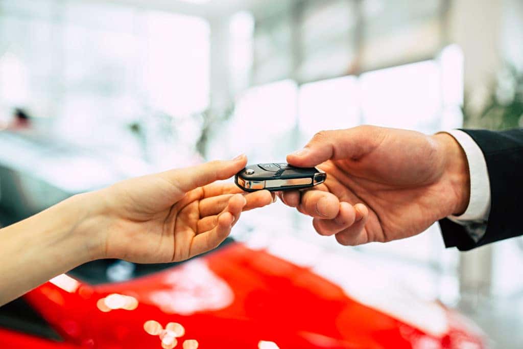 hands exchanging car keys in dealership showroom
