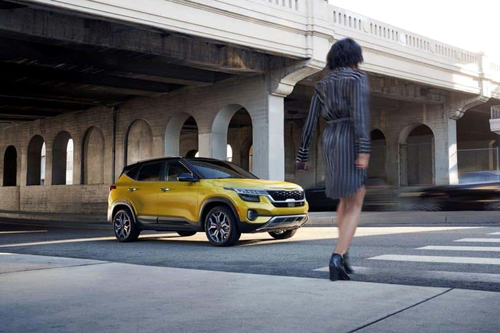 Gold Kia Seltos SUV on city street with person walking across street