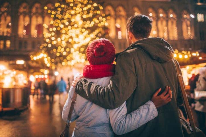 couple staring at a lit Christmas tree outside