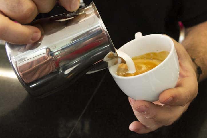 barista's hand drawing a picture on the latte cup