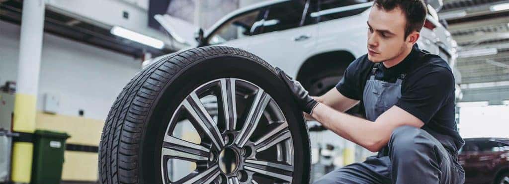 Mechanic exams a car tire before mounting it on a raised vehicle