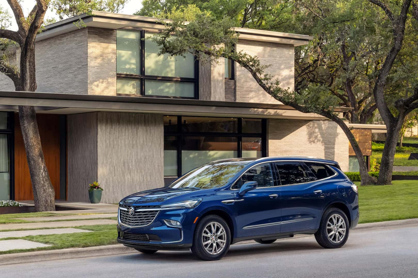 Driver front 3/4 view of 2023 Buick Enclave in Emperor Blue Metallic parked curbside with house in background.