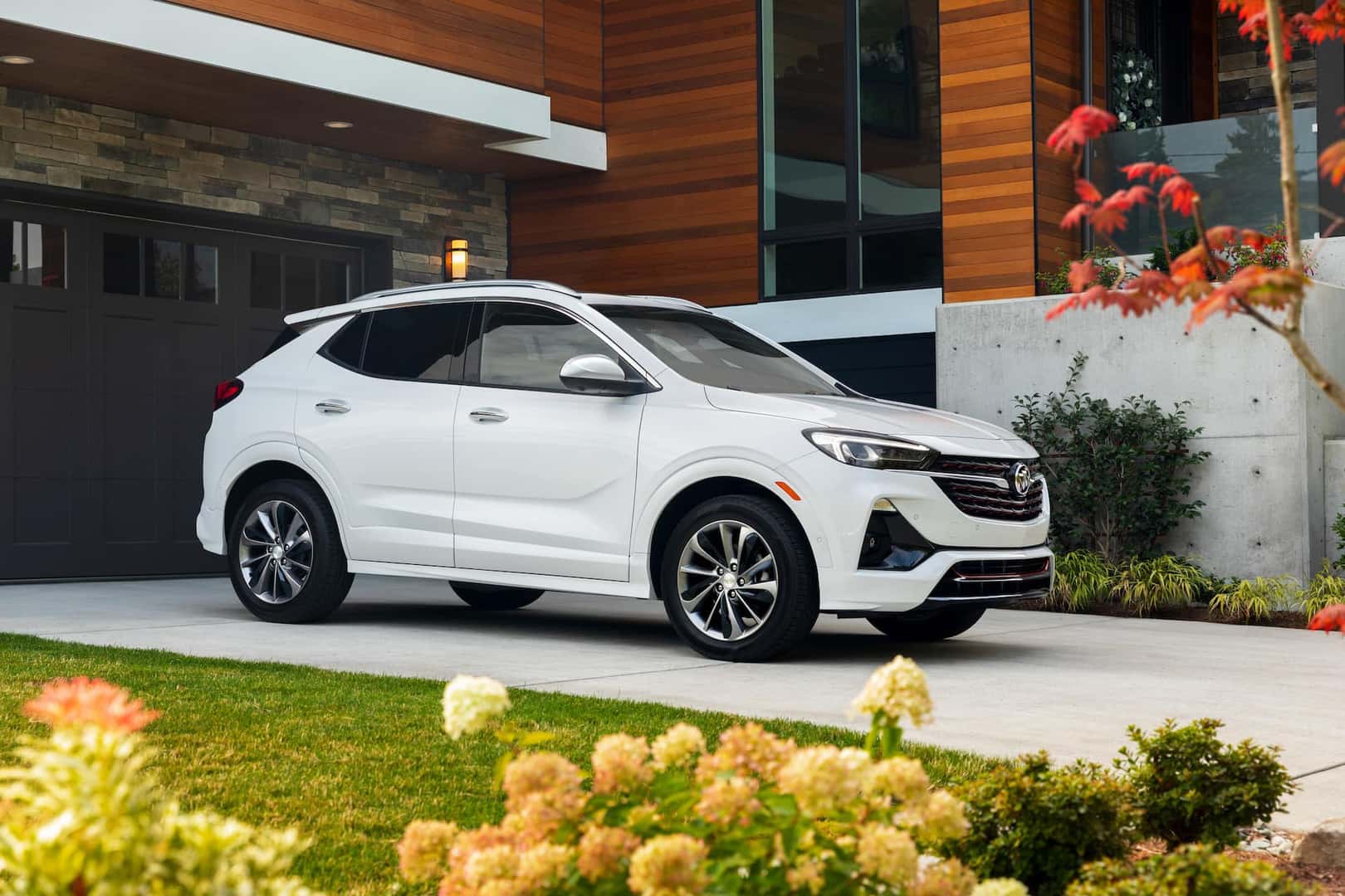 Passenger front 3/4 view of 2023 Buick Encore GX in White Frost Tricoat parked in the driveway of a home