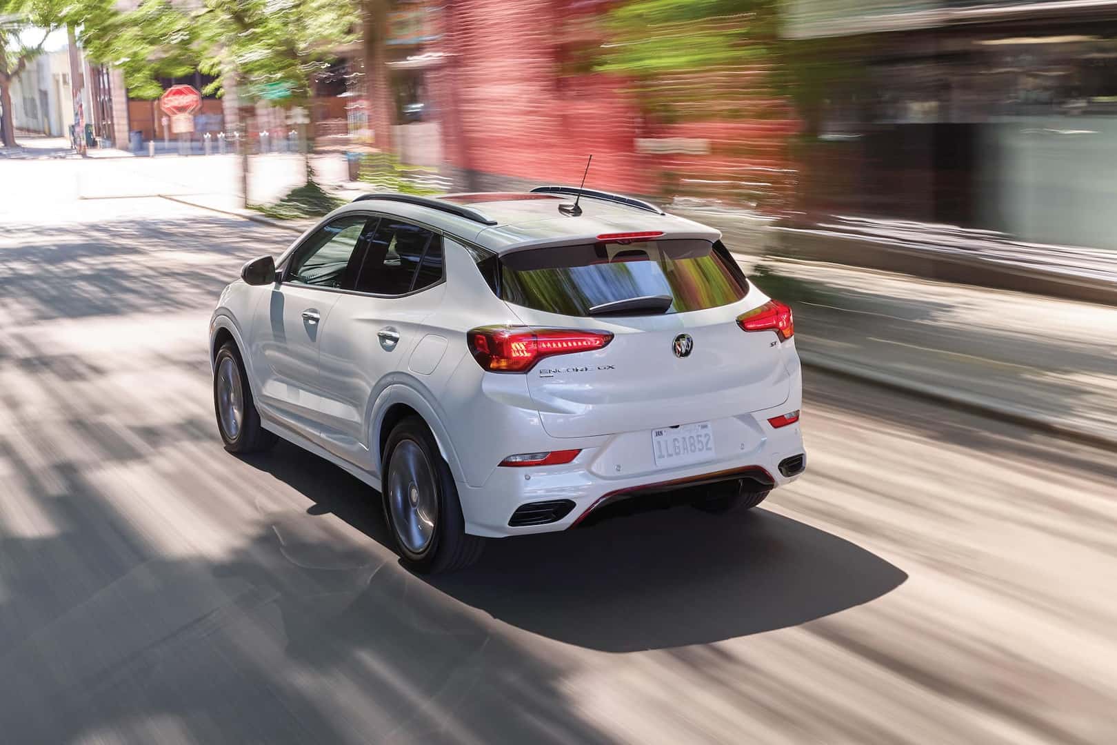 Driver rear 3/4 view of 2023 Buick Encore GX in White Frost Tricoat driving on road