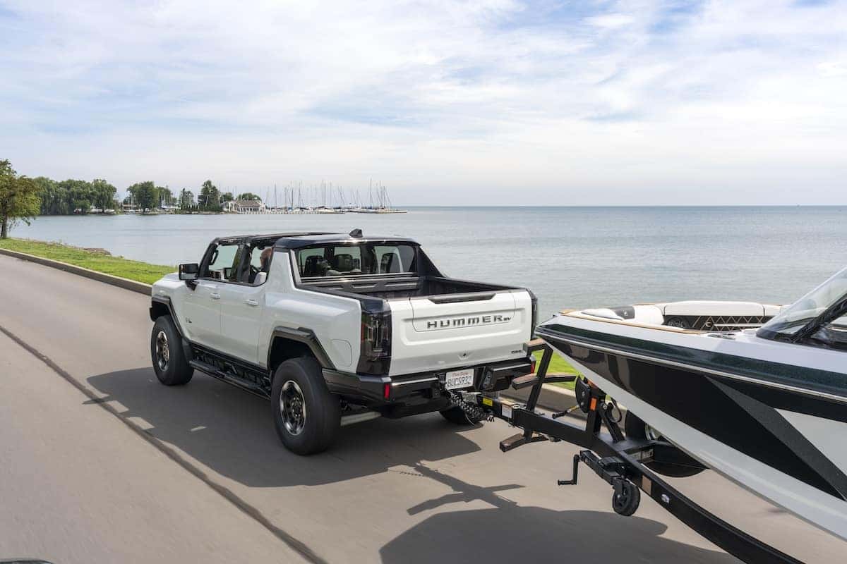 Overhead and rear 3/4 view of the 2023 GMC HUMMER EV Edition 1 Pickup towing a Super Air Nautique GS22E electric boat on the road.